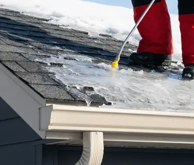 Ice dam removal technician using a steam wand to melt thick ice buildup on a residential roof in Des Moines, IA